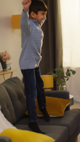 Vertical-Video-Of-Disruptive-Young-Boy-Behaving-Badly-At-Home-Jumping-On-Sofa